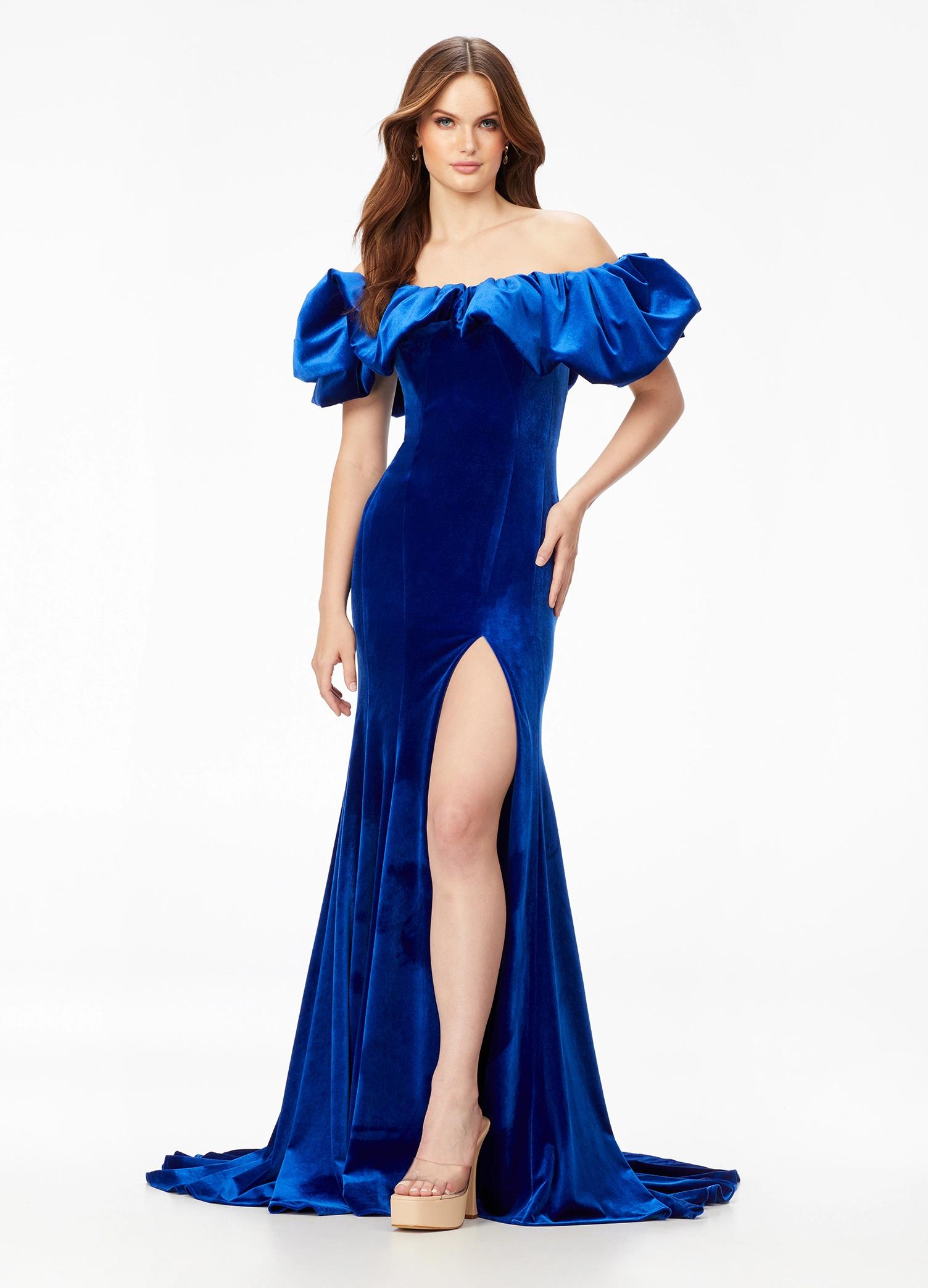 Blue ASHLEYlauren 11217 – A magnificent off-shoulder velvet gown featuring oversized ruffle details, a contour seamed skirt with a left leg slit, and a dramatic train. Perfect for making a bold, elegant statement at any event.